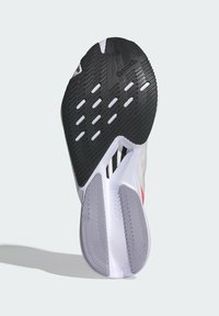 Suela de goma negra con surcos y patrones de tracción, entresuela blanca y parte superior de textil transpirable con detalles en rojo y logotipos.
