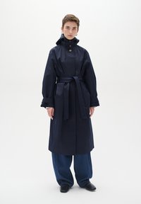 Jūras karaflotes ūdensizturīgs trenčkotis ar augstu apkakli, pogu akcentiem un vidukļa saitēm. Brīvi pieguļoši džinsi un melni apavi pabeidz izskatu.