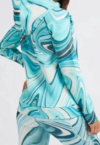 Top de ocio con capucha que presenta un diseño en espiral de color turquesa y blanco, con una textura suave y elástica y acentos oscuros contrastantes.