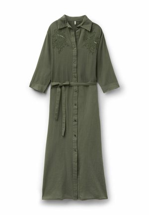Longue robe boutonnée vert olive avec manches trois-quarts, détails brodés sur la poitrine, et ceinture en tissu nouée à la taille.