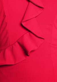 Gros plan sur un tissu rouge vif avec un détail froncé le long d'une couture, montrant une texture douce et des plis.
