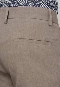 Pantaloni marroni chiari con una leggera texture, dotati di una tasca posteriore posizionata sul lato destro e un design della vita piatta.