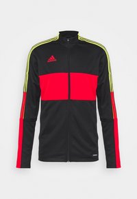 Chaqueta de chándal negra con acentos en rojo y amarillo neón, cierre de cremallera y tres rayas en los hombros. Fabricada con un tejido suave y ligero.