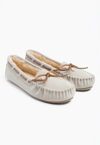 Pantuflas de mocasín de ante beige con un suave forro de piel, cordones de cuero y un detalle de costura fruncida a lo largo del borde superior. Suela plana.