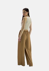 Top corto beige e pantaloni ampi e leggeri di colore marrone chiaro, con vita elastica e tessuto testurizzato, visti da dietro.