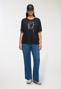 Czarna, krótki rękaw T-shirt z białym rysunkiem twarzy, zestawiony z niebieskimi, dżinsowymi spodniami z szerokimi nogawkami i czapką w kolorze czarnym. W komplecie obuwie casualowe.