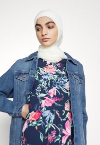 Jaqueta de ganga com um corte clássico sobre um vestido floral azul-marinho com padrões em rosa, azul e verde; o lenço branco completa o visual.