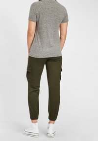 Šedá košile s krátkým rukávem, olivově zelené jogger kalhoty s bočními kapsami a elastickými manžetami, doplněné bílými teniskami. Jednoduchý a neformální design.