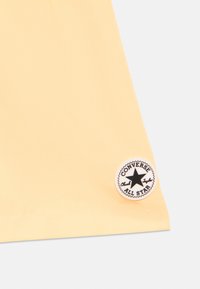 Κίτρινο ύφασμα με στρογγυλό λευκό τμήμα που περιέχει μαύρο κείμενο και σχέδιο αστεριού, με την ετικέτα «Converse Chuck Taylor All Star».