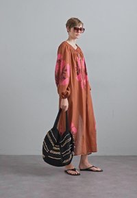 Καφέ φλοράλ φόρεμα με ροζ λεπτομέρειες, άνετη εφαρμογή και μακριά μανίκια; αξεσουάρ με μία μαύρη πλεκτή τσάντα με χρυσά σχέδια και σαγιονάρες.