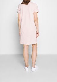 Light pink short-sleeve dress with a straight cut, made from smooth fabric, reaching mid-thigh; paired with white sneakers.