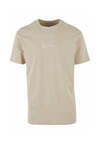 Tricou din bumbac bej cu guler rotund, mâneci scurte și un logo alb cu text pe partea superioară stângă a pieptului. Textură netedă, design simplu.