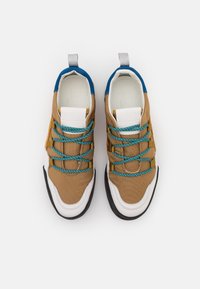 Paire de baskets marron, blanc et bleu avec des lacets turquoise, vues de dessus sur un fond blanc.