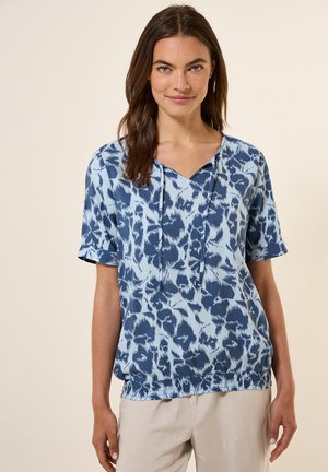 Korte mouwen blauwe top met een v-hals, trekkoorddetail en een gestructureerd, abstract patroon in verschillende tinten blauw en wit.