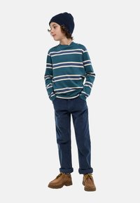 Chemise à manches longues rayée en bleu sarcelle avec des rayures blanches et crème, associée à un pantalon bleu marine et des bottes à lacets marron.