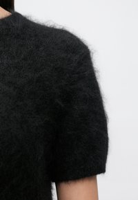 Pulover negru cu mâneci scurte din material tricotat moale, cu guler rotund și aspect texturat.