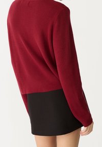 Cropped, ribbed red sweater with long sleeves, features a round neckline and a straight cut, paired with a black mini skirt.