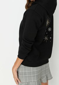 Sudadera negra con un acabado texturizado, con diseños coloridos de estallidos de estrellas. Combinada con una falda acampanada de cuadros grises.
