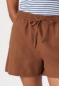 Brune bomullsshorts med elastisk midje og snor. Stoffet har en myk tekstur og en avslappet passform.