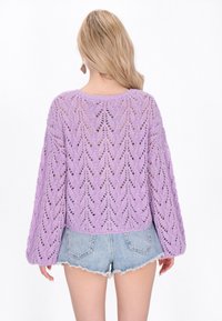 Pulover tricotat lila, cu o croială lejeră, lucrat în dantelă cu model și mâneci largi, asortat cu șorturi din denim destramate.