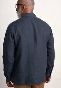Camicia di lino blu scuro con colletto e polsini abbottonati, caratterizzata da una vestibilità morbida e un tessuto testurizzato, vista dal retro.