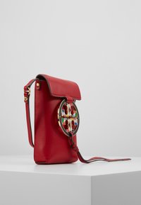 Rød læder crossbody taske med en klap, guldfarvet cirkulær hardware og flerfarvede geometriske accenter. Har en tynd justerbar rem.