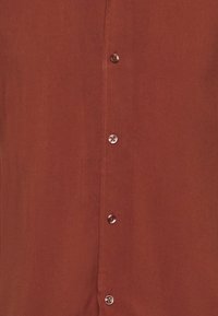 Πουκάμισο χρώματος σκουριάς με κουμπιά, φτιαγμένο από απαλό ύφασμα, με σειρά από κουμπιά στο ίδιο χρώμα και απλό, καθαρό σχέδιο.