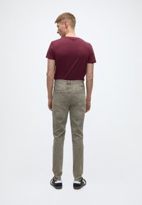 Tamsiai raudona aptempta marškinėlių ir šviesiai pilkos kelnės, pagamintos iš minkštos medžiagos, su klasikine liemens juosta ir standartinėmis galinėmis kišenėmis.