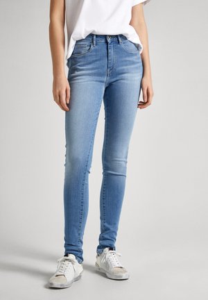 Světle modré džíny skinny s středním pasem, pěti kapsami, jemně blednoucí a hladkou texturou, nošené s bílými teniskami.