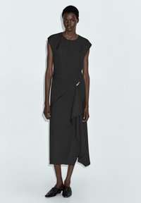 Schwarzes, knielanges Kleid mit kurzen Ärmeln, drapiertem Design und seitlichem Twist-Akzent; strukturierter Stoff mit glatter Oberfläche.