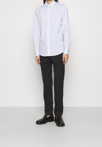 Camicia a maniche lunghe a righe blu chiaro e bianche con chiusura a bottoni, abbinata a pantaloni neri a gamba dritta e scarpe slip-on nere.