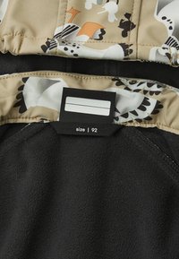 Svart fleece tyg med beige kant som har abstrakta fågelmönster och en svart storleksmärkning märkt "storlek | 92."