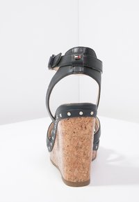 Czarne skórzane sandały na koturnie z korkowym obcasem, regulowany pasek i srebrne ćwieki. Logo umieszczone na pasku.