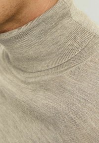 Jasno beżowy sweter z golfem, wyróżniający się prążkowanym kołnierzem i gładką, miękką teksturą. Tkanina ma subtelny, nieco nierówny wzór.
