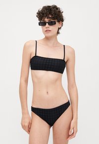 Black bikini set featuring a strapless top with a textured pattern and matching low-rise bottoms. Materials appear smooth with thin straps.