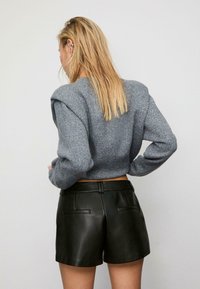 Maglione grigio cropped con tessuto testurizzato e maniche a sbuffo, abbinato a pantaloni corti in pelle nera a vita alta con due tasche posteriori.