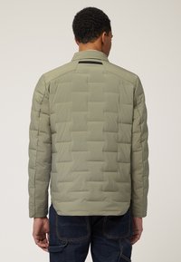 Maslinasto zeleni puffer jakna s kvadriranim dizajnom, čvrste teksture i ravnim krojem. Ima uski ovratnik i bez vidljivih dodataka.