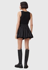 Zwarte mouwloze top gecombineerd met een uitlopende zwarte mini rok en kniehoge zwarte leren laarzen; gladde textuur met een aansluitend ontwerp.