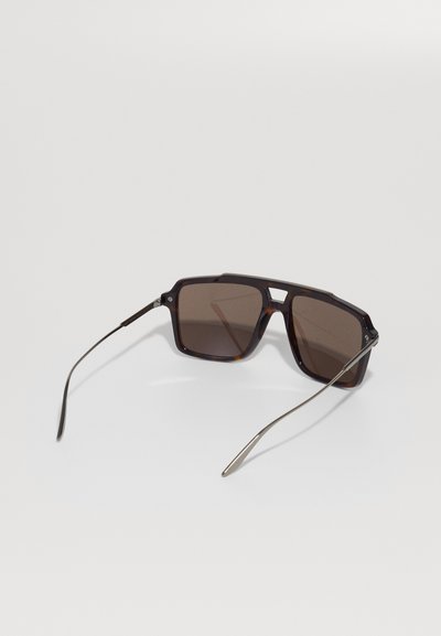Ochelari de soare cu un cadru din plastic texturat, de culoare tortoiseshell închis și lentile maro. Temele subțiri din metal și un design geometric. Textură netedă și lucioasă.