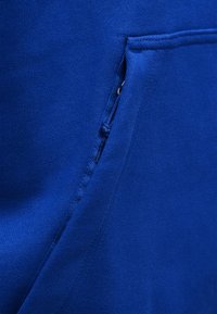 Κον τινό πλάνο μπλε υφασμάτινης τσέπης με ορατή ραφή και μικρό τμήμα φερμουάρ εν μέρει κρυμμένο στη ραφή.