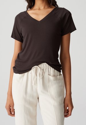 Kvinde iført en sort kortærmet V-hals top, der er let stukket ind i off-white snørede bukser med sidelommer.