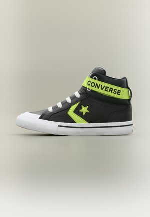 Melns Converse augstpapēžu kedas ar baltu zoli un šņorēm, neona zaļu zvaigzni un ķebura dizainu, kā arī neona zaļu siksnu ar uzrakstu "CONVERSE".
