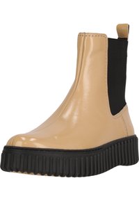 Bottines en vernis beige avec des panneaux latéraux élastiques noirs et une semelle en caoutchouc noir texturé. Surface lisse avec un bout arrondi.