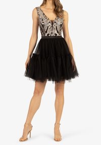 Robe en tulle noire avec un corsage ajusté, ornée de détails argentés et d'un décolleté en V profond. Jupe évasée à plusieurs couches avec un ourlet froncé.