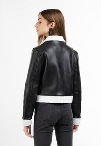Sort læderjakke med hvidt shearling-krave og -manchetter, cropped design, der har en glat tekstur og en tætsiddende silhuet.