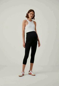 Svarte capri leggings med høy midje, kombinert med en hvit ermeløs topp, og hvite sneakers med røde detaljer. Glatt tekstur.