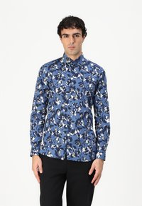 Camicia floreale blu con maniche lunghe, colletto button-down, caratterizzata da un motivo di fiori bianchi e blu scuro su uno sfondo blu chiaro.