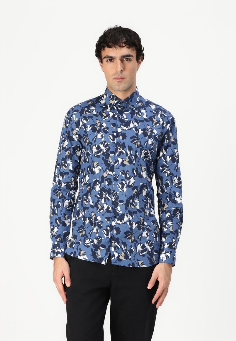 Camicia floreale blu con maniche lunghe, colletto button-down, caratterizzata da un motivo di fiori bianchi e blu scuro su uno sfondo blu chiaro.
