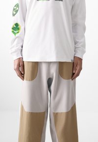 Long-sleeve white shirt with green leaf graphics on sleeves; light gray pants with brown pocket accents, made of soft, textured material.
