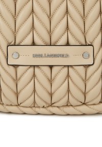 Geanta din piele bej, captusita, cu un design impletit si accente netede, avand o placa pe care este inscriptionat "KARL LAGERFELD" in argintiu.